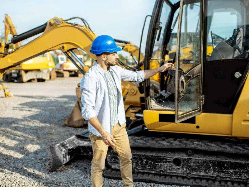 Hombre inspeccionando maquinaria pesada usada, evaluando si debe elegir entre maquinaria nueva o usada para su proyecto de construcción.