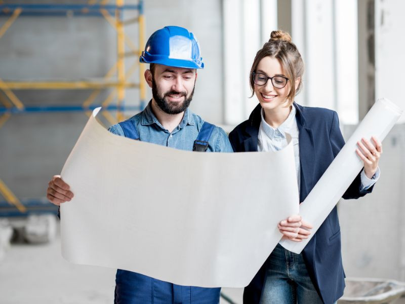 Dos ingenieros observando planos de construcción, analizando la viabilidad de alquilar maquinaria pesada para proyectos de corta duración.