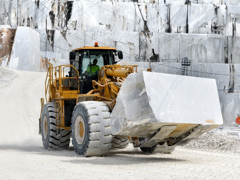 Excavadora pesada cargando grandes bloques de piedra en una cantera, representando la compra de maquinaria para proyectos de larga duración.