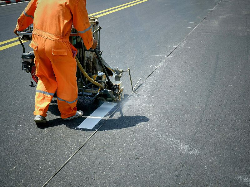 Trabajador aplicando señalización vial en una carretera recién pavimentada.