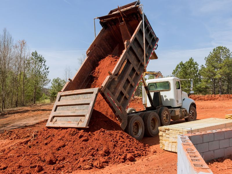 Camión volquete descargando tierra en una obra de construcción, utilizado para el transporte de grandes volúmenes de material.