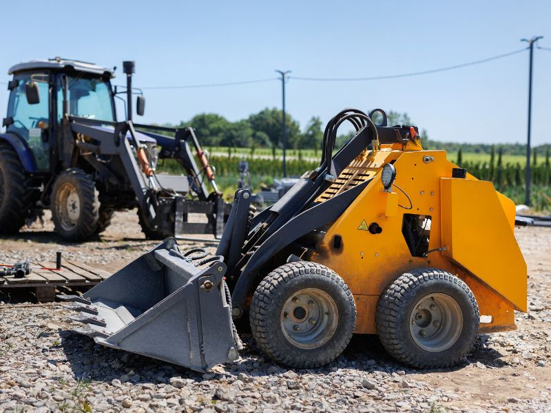 Minicargador compacto estacionado en un sitio de construcción, utilizado para movimientos de tierra en espacios reducidos.