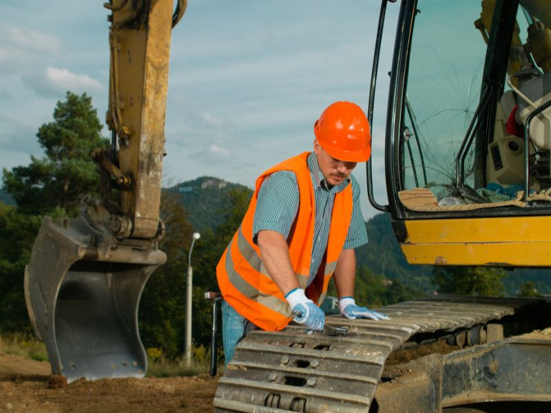 Hombre realizando el mantenimiento de la oruga de una excavadora hidraulica